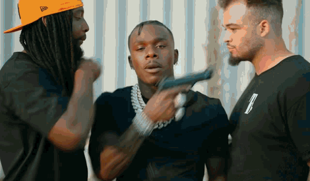 a man with dreadlocks is holding a gun while two other men look on