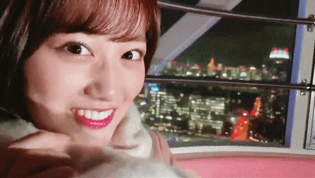 a woman smiles while looking out of a ferris wheel at night