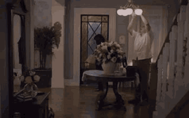 a man is fixing a light fixture in a living room while a woman looks on .