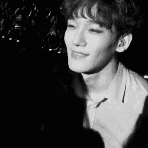 a black and white photo of a young man covering his mouth with his hand while singing into a microphone .