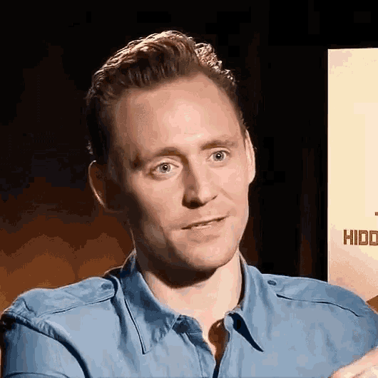 a man in a blue shirt is making a funny face while sitting in front of a sign .