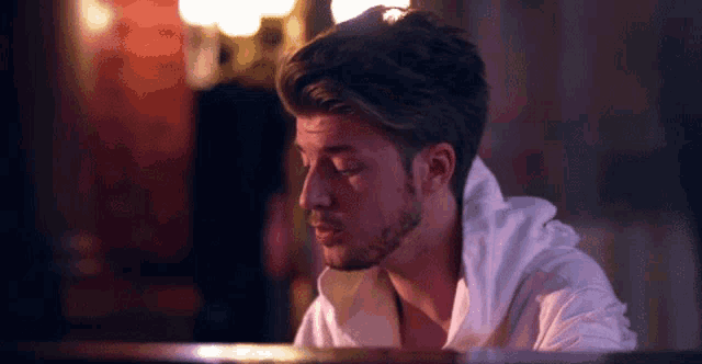 a man with a beard and a white shirt is sitting at a piano