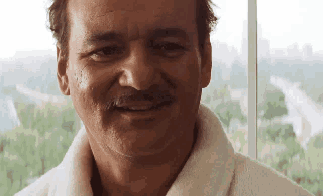 a man with a mustache wearing a white robe smiles for the camera