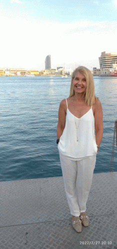 a woman in a white tank top and white pants stands in front of the water