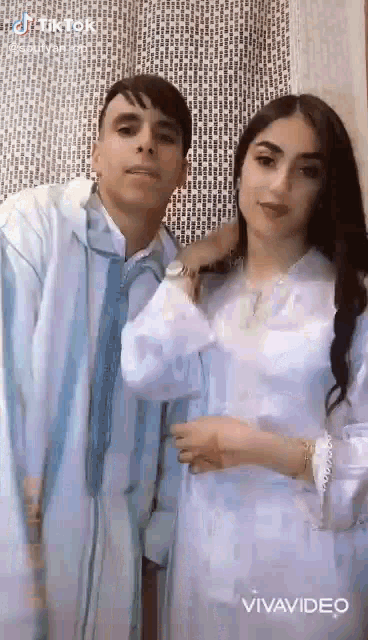 a man and a woman are posing for a picture together . the woman is wearing a white dress .