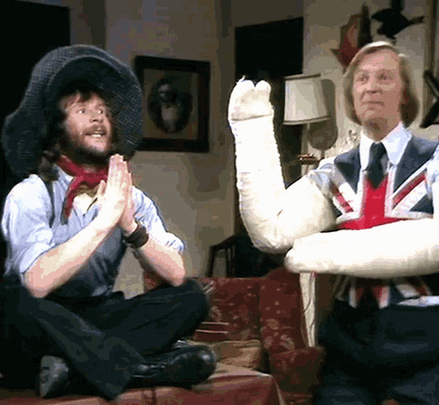 two men are sitting on a couch with one wearing a british flag vest