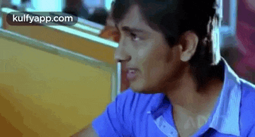 a man in a blue shirt is sitting at a table in a restaurant and making a funny face .