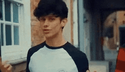 a young man wearing a black and white shirt is standing in front of a window .