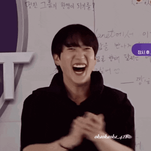 a young man is laughing in front of a white board with foreign writing on it