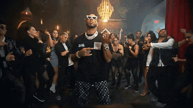 a man wearing sunglasses stands in front of a crowd of people at a party