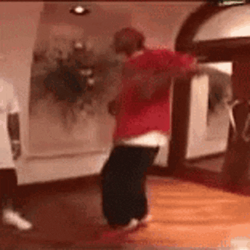 a man in a red shirt and black pants is dancing in a room in front of a mirror .