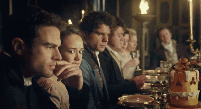 a group of people sitting at a table with a cake in the middle