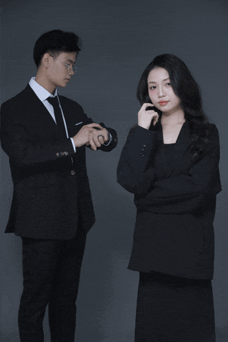 a man and a woman are standing next to each other and the man is pointing at his watch