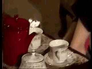 a woman is sitting at a table with two cups of coffee and a sugar bowl .