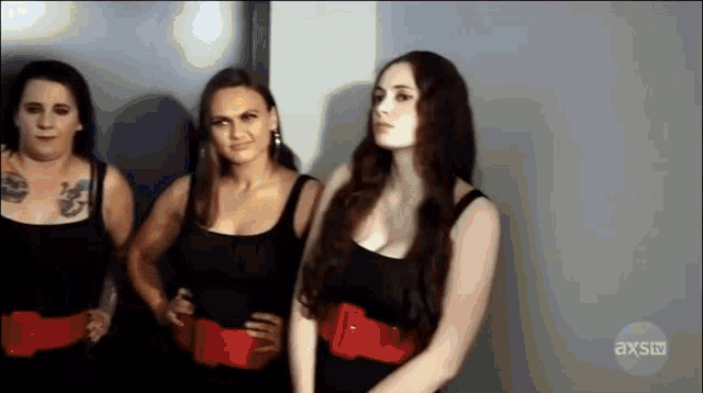 three women wearing black tank tops and red belts are standing next to each other in front of an axs tv logo
