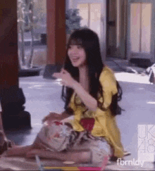 a woman in a yellow dress is sitting on the floor and laughing .