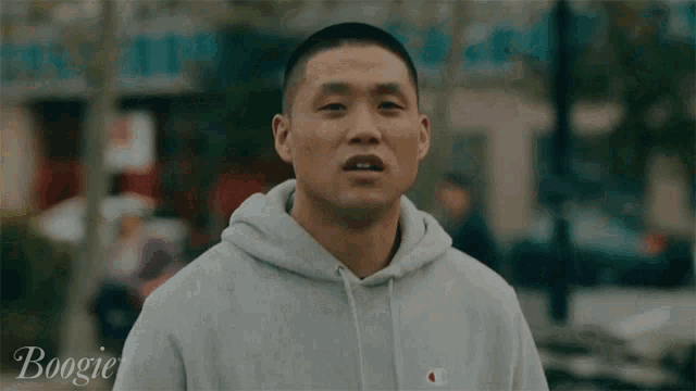 a man in a grey hoodie is standing in front of a building that says boogie