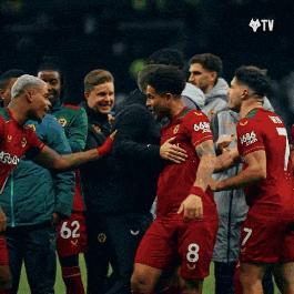 a man in a black jacket is standing in front of a group of soccer players wearing red uniforms .