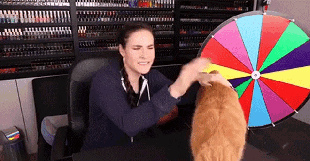 a woman is playing with a cat in front of a colorful wheel of fortune .