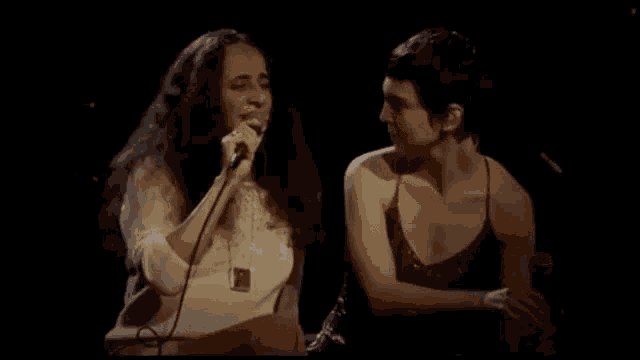 a woman is singing into a microphone while sitting next to another woman .