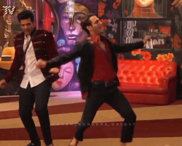 two men are dancing in front of a red couch and a sign that says ' galaxy ' on it