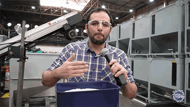 a man in a plaid shirt is holding a microphone in front of a blue container