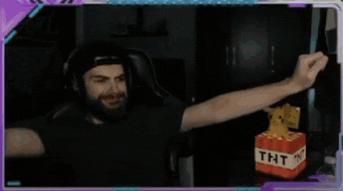 a man is sitting in a chair with his arms in the air and a tnt block in front of him