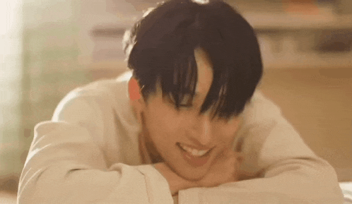 a young man is laying on a bed with his head on his hands .