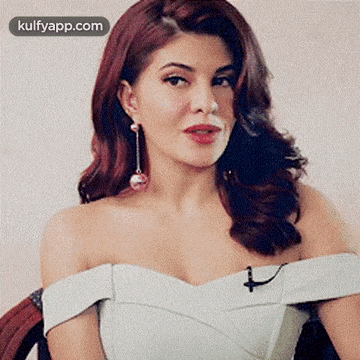 a woman with red hair is wearing a white dress and earrings .
