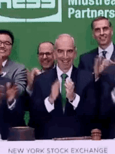 a group of men clapping in front of a new york stock exchange table
