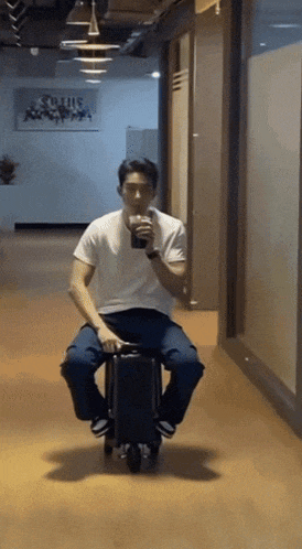 a man is sitting on a suitcase in a hallway and drinking from a cup