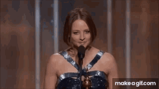 a woman in a blue dress is speaking into a microphone and smiling .