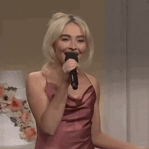 a woman in a pink dress is singing into a microphone and smiling .