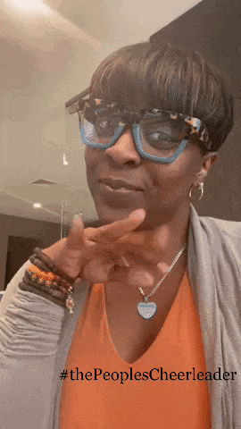 a woman wearing glasses and a necklace has the hashtag #thepeoplescheerleader