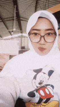 a woman wearing glasses and a white hijab is wearing a mickey mouse shirt