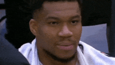 a basketball player is sitting in the stands during a game and smiling .