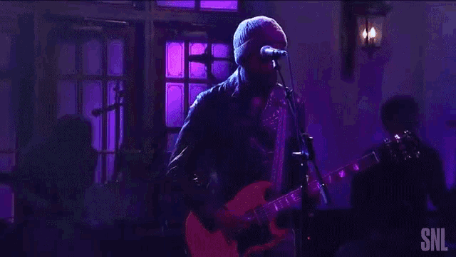 a man playing a guitar and singing into a microphone with snl written on the screen