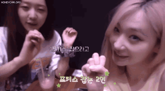 two girls are sitting at a table with korean writing on the bottom of the screen