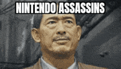 a man with a beard is standing in front of a building with the words `` nintendo assassins '' above him .