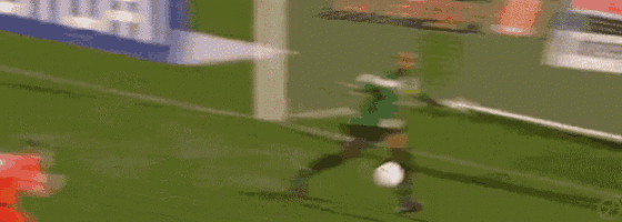 a blurry picture of a soccer game with a goalie and a soccer player in red .