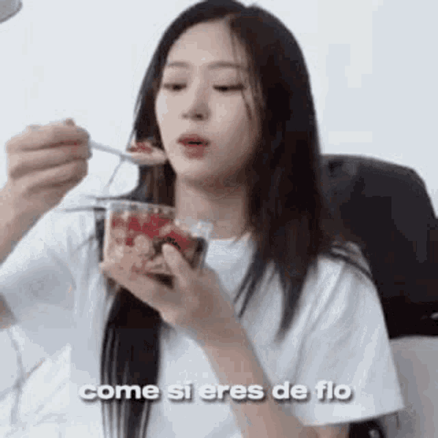 a woman is eating a dessert with a spoon and a cup of strawberries .