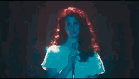 a woman with red hair is standing in a dark room with a blue light behind her .
