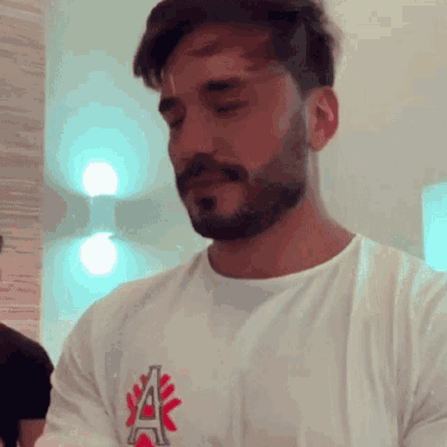 a man with a beard is wearing a white shirt with the letter a on it .