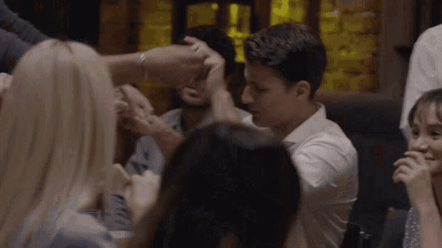 a group of people are sitting around a table and one of them is holding another man 's hand