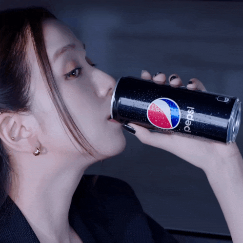a woman is drinking a can of pepsi from her hand