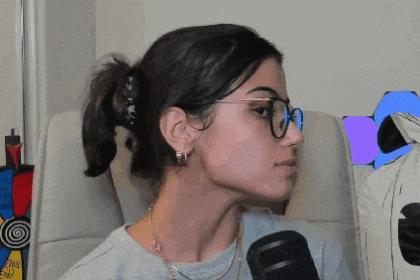 a woman wearing glasses is sitting in front of a microphone and pointing to her ear