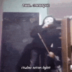a woman in a mask is holding a broom in front of a chalkboard with russian writing on it .