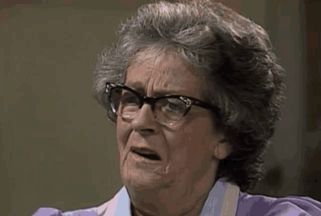 a close up of an elderly woman wearing glasses and an apron making a funny face .