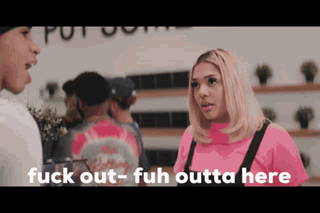 a woman in a pink shirt is talking to a man in a store and the woman is saying fuck out-fuh outta here