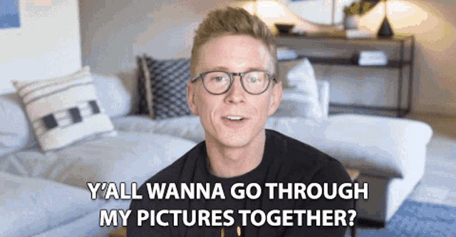 a man wearing glasses is sitting in a living room with the words y'all wanna go through my pictures together